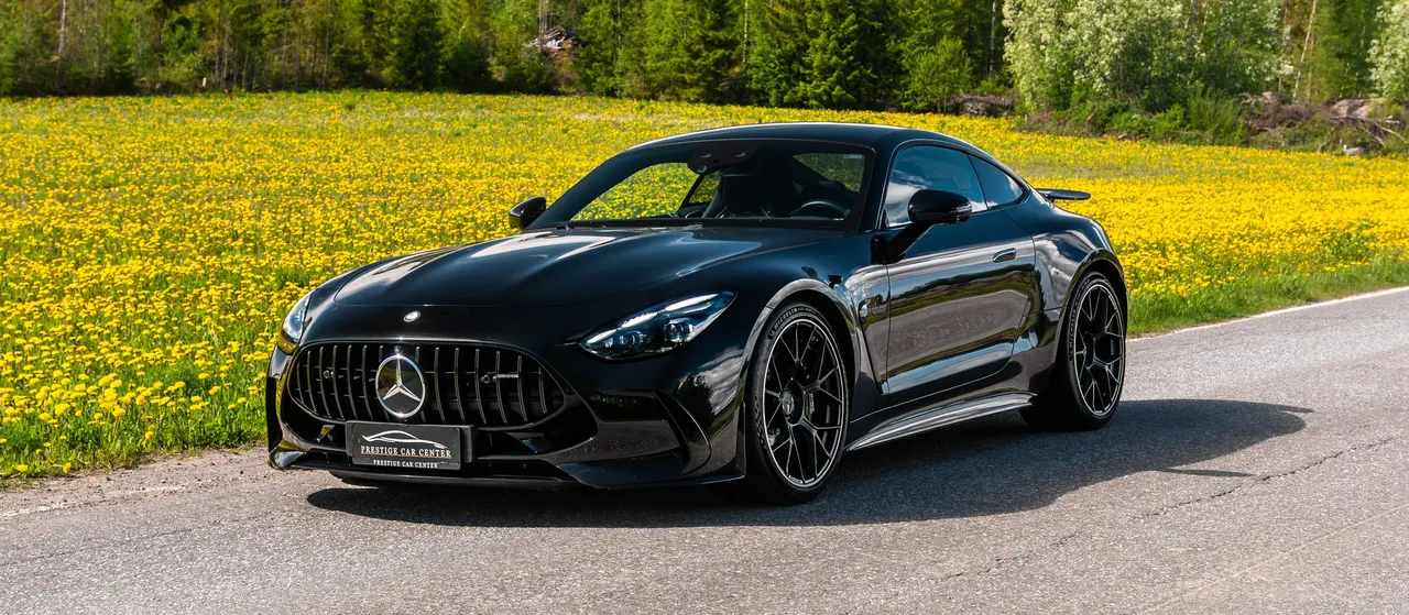 Musta Mercedes-AMG GT maantiellä kesämaiseman keskellä
